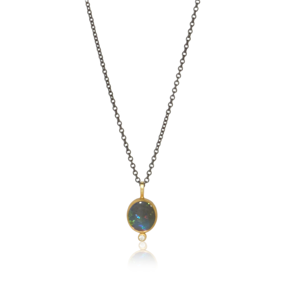 shows an opal set in gold with a diamond at the bottom on a black chain
